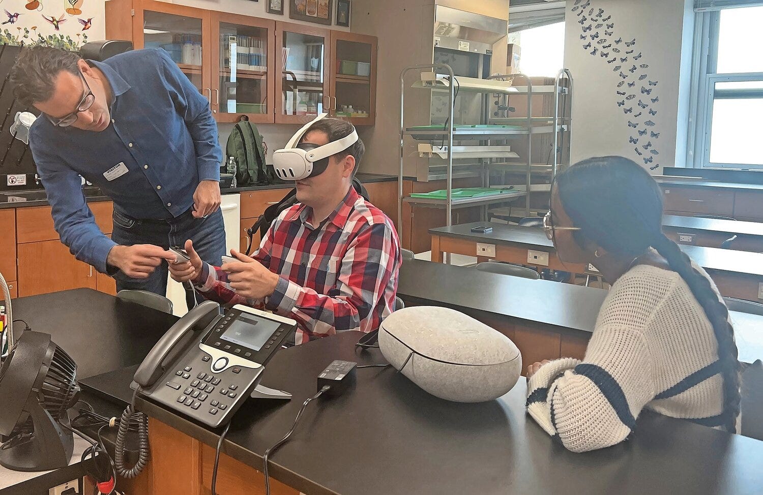 Jase Bernhardt in a classroom with two high school students testing the driving simulator. 