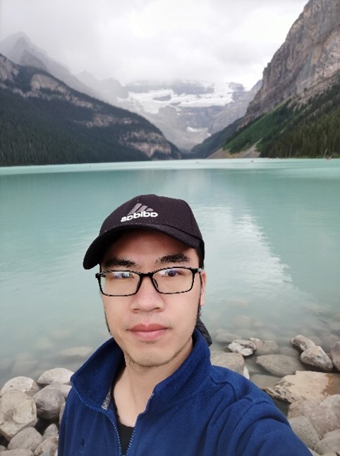 Guoqiang Tang standing in front of a lake, with mountains in the background, at Banff National Park.