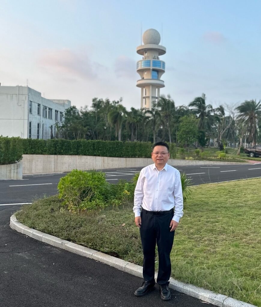 Kun Zhao standing outside, with trees, a building, and a radar tower in the background.