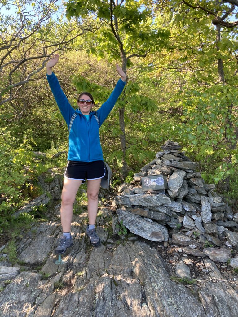 A photo of Natalie Umphlett standing on the south slope of Mount Frissell in Connecticut, the state's highest point. 
