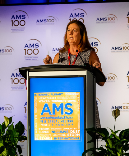 A photo of Jenni Evans as AMS President-Elect in front of a podium speaking at the AMS 99th Annual Meeting in Phoenix, Arizona.