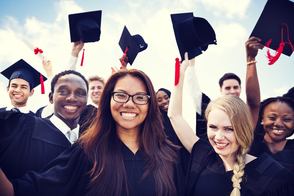 Students in graduation garb smiling and holding up their caps