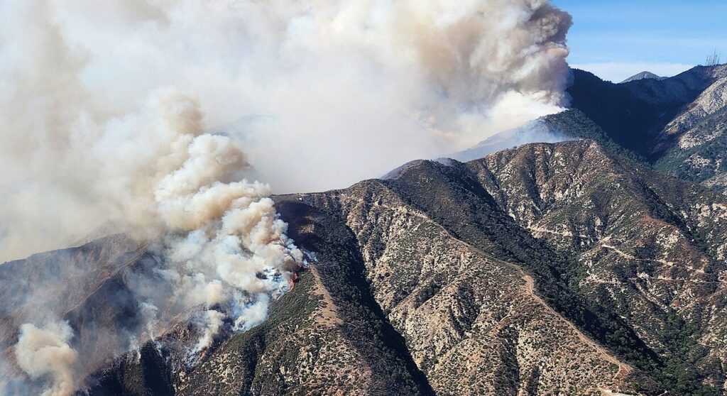 Smoke and fire near the top of a mountain during the day.