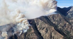 Smoke and fire near the top of a mountain during the day.