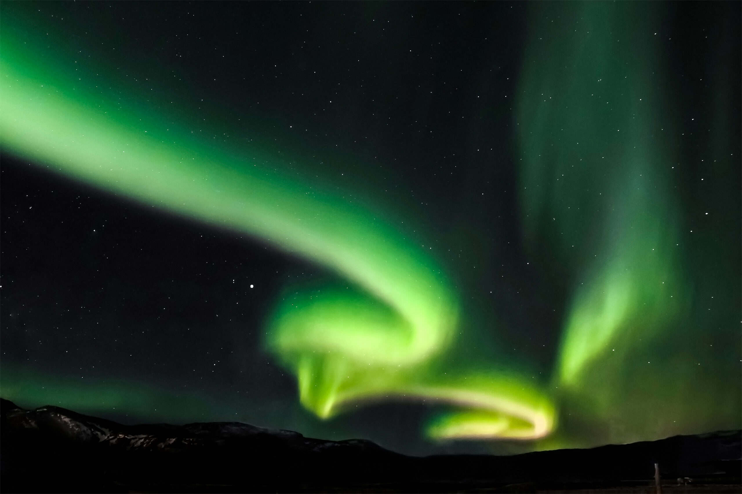 In faraway Iceland a colorful aurora lights up the night sky. In the right low corner is an Icelandic horse.